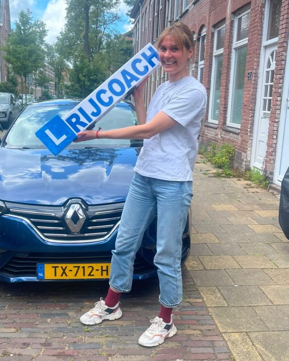 Geslaagde leerling in Haarlem met Rijcoach bord bij de lesauto