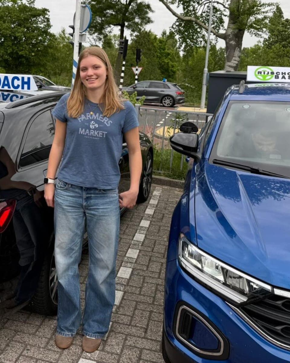 Geslaagde leerling bij Rijcoach Haarlem naast een blauwe lesauto