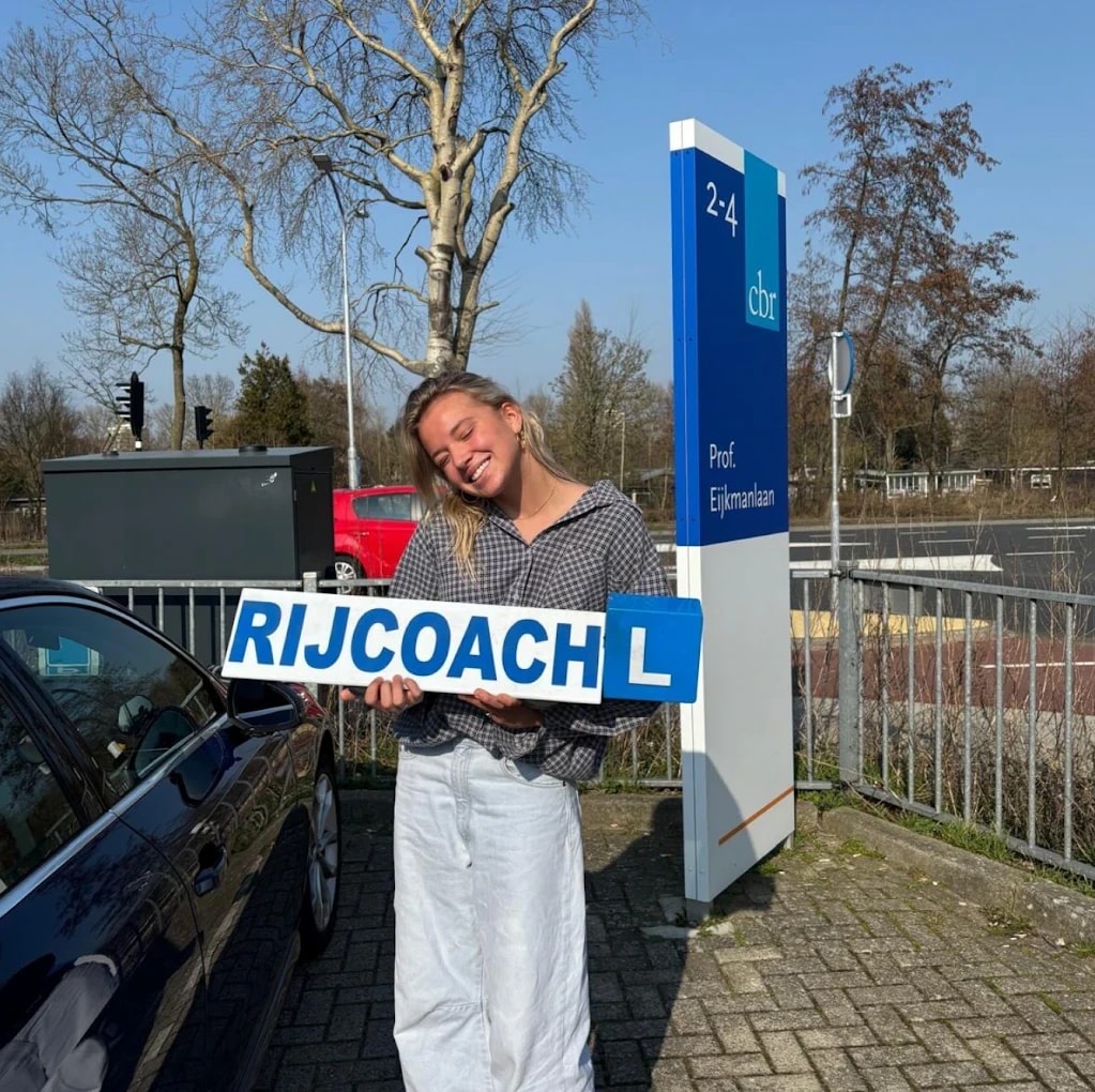Lachende leerling houdt het Rijcoach-lesbord vast voor het CBR-examencentrum in Haarlem