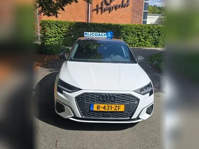 Witte Audi A3 lesauto van Rijcoach met dakbord, herkenbare Audi-grille en kenteken voor College Hageveld in Heemstede